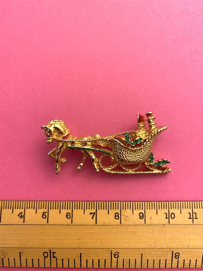 image of a vintage brooch depicting a sleigh and horse with ruler for measurement