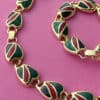 Image shows a top view of a Vintage 1980s Necklace & Bracelet Set in Gold with Red Green Black Enamel on a hot pink background